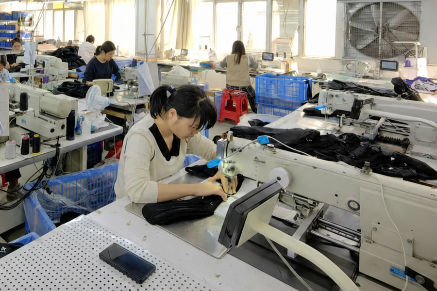 Operator sewing black textile bag panels at an industrial workstation